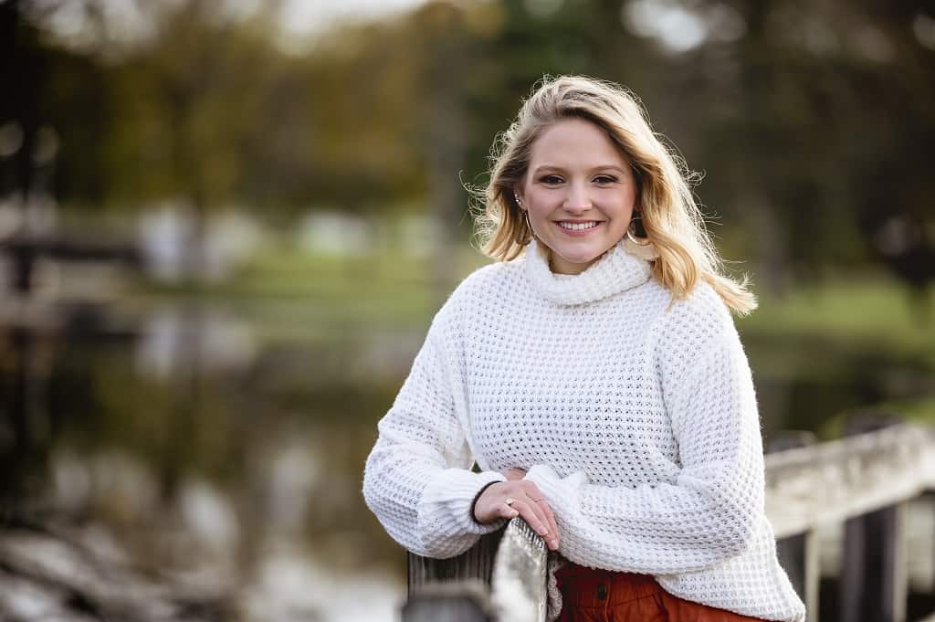 A shallow focus shot of a female leaning against a wooden fence and smiling at the camera