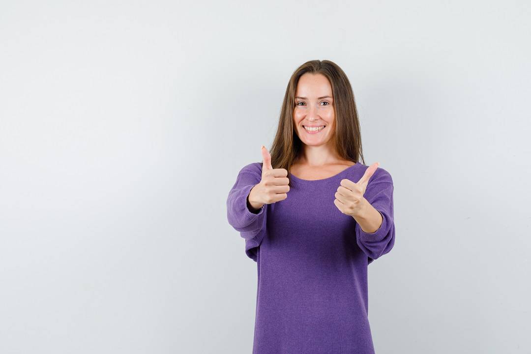 Young girl showing thumbs up in violet shirt and looking optimistic , front view.