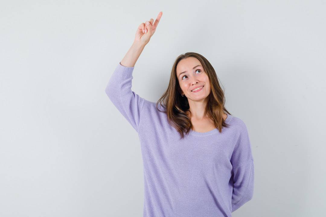 young woman in lilac blouse pointing up and looking happy , front view.